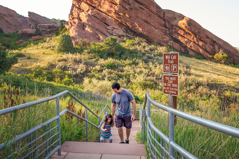 A father has fun helping his toddler daughter who is jumping up the stairs at Red Rock Park, Colorado.